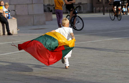 A child carries a fluttering tricolor Lithuanian flag outdoors. Kaunas Lithuaniaのeditorial素材
