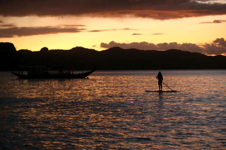 A silhouette photo of a young girl on a standing paddle. Active holidays, life on the beach....