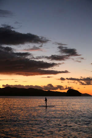 A silhouette photo of a young girl on a standing paddle. Active holidays, life on the beach....