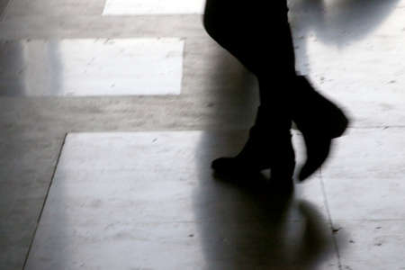 Dark silhouettes of the legs of four walking on the side walk in bright backlight, Italy Milan