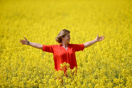 A happy young woman in a red dress enjoys summer in a rape field. Rural landscape with an oil field. Spring colored flower and oil oil.の写真素材