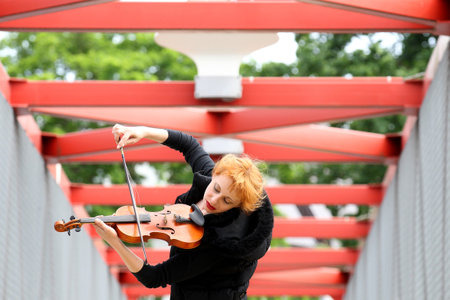 An emotional woman playing the violin on a red bridgeの写真素材