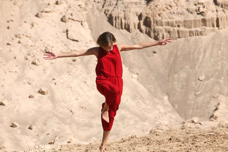 A young happy, barefoot woman in red posing in a sand careerの写真素材