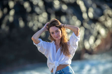 Awesome portrait of a young calm girl with long hair against a faint rocky blue sea background.の写真素材