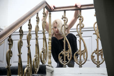 A young blonde woman in a black blues poses on an old staircase near a decorated railingの写真素材