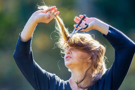 A young woman is cutting her hair, an act of protestの写真素材