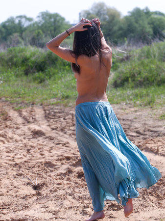 A beautiful young woman in a stylish long light silk skirt poses in natureの写真素材