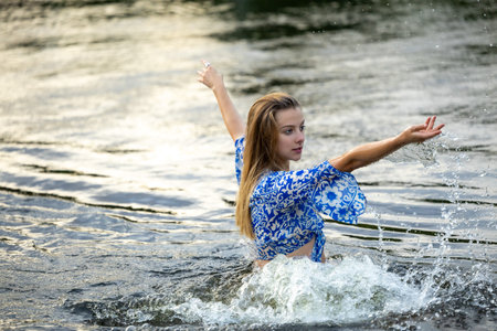 A young girl splashing in the river water on a hot summer eveningの写真素材