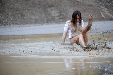A woman in a white blouse expresses her emotions in a muddy puddleの写真素材