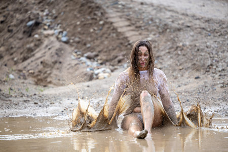 A woman in a white blouse expresses her emotions in a muddy puddleの写真素材