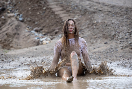 A woman in a white blouse expresses her emotions in a muddy puddleの写真素材