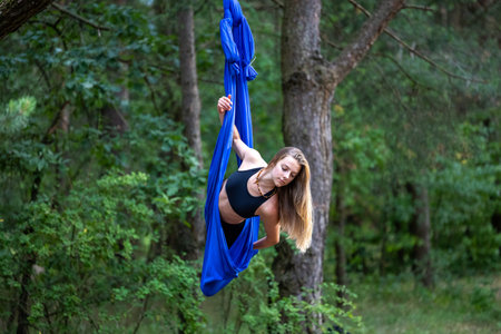 Young woman doing antigravity yoga exercises with aerial silk in the park.の写真素材