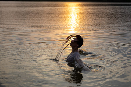 Young pretty girl relaxing bath in lake before golden sunset