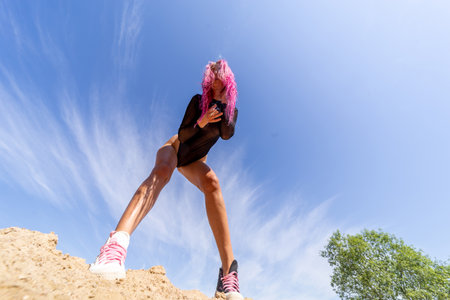 Extravagant girl with red hair, black bodysuit and cigarette against blue sky backgroundの写真素材