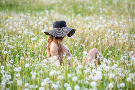 Beautiful young woman with a hat in a dandelion meadowの写真素材