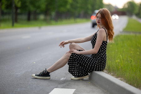 Young beautiful red hair hipster woman sitting on the curb in the city