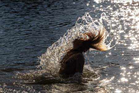 A young woman with long hair in the water at sunset creates a lively and warm scene, the concept of swimmingの写真素材