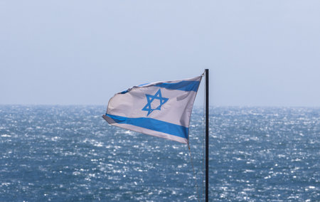 National flag of Israel waving in the wind against the background of sea and sky