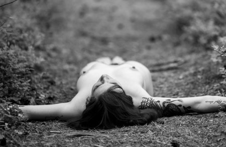 A beautiful, bold dark-haired girl. Posing while lying on a forest trackの写真素材