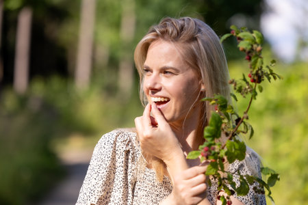 Young beautiful woman eating wild raspberries in the forest