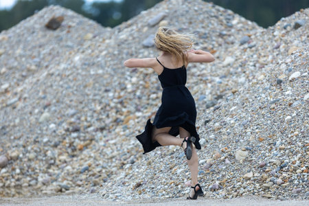 Young beautiful woman in black dress and sand quarry background, in motionの写真素材