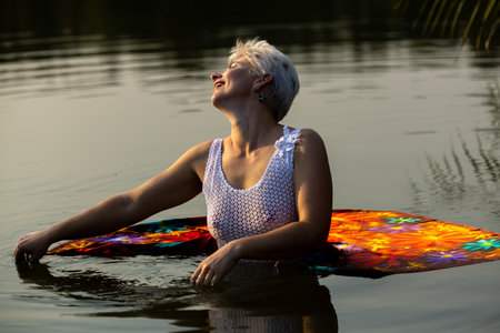 An older woman enjoys the calm water in evening light. With a colorful scarfの写真素材