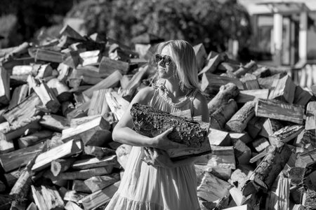 A cheerful woman gathers firewood under the bright sun, embracing the warmth and tranquility of...