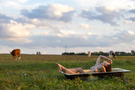 A Beautiful Woman Relaxing in Natures Bathtub, Surrounded by Grazing Cowsの写真素材