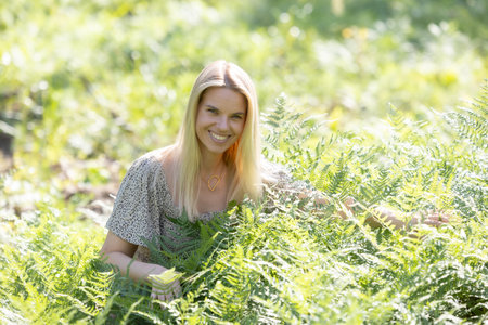 A beautiful woman enjoying the summer warmth: a smile among the greenery, embraced by fernsの写真素材