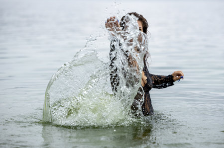 Woman in Black Attire Splashing in Water: Elegance Meets Natureの写真素材