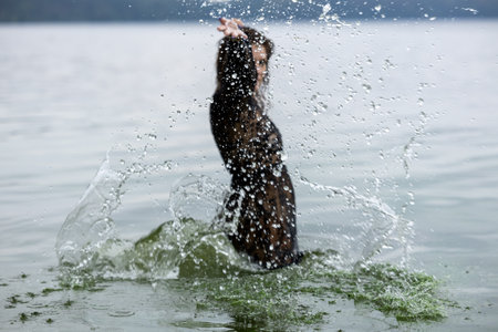 Woman in Black Attire Splashing in Water: Elegance Meets Natureの写真素材