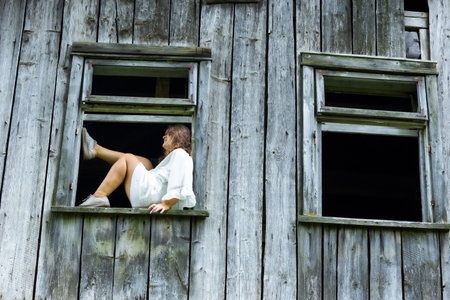Modern Elegance in a Historic Window: A Woman Posing in an Old House, Surrounded by Memoriesの写真素材