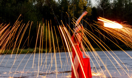 Young beautiful woman in a red dress performing an extreme fire show with falling sparks