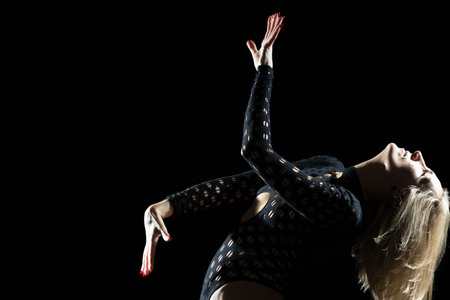 The Aesthetics of Dance in the Studio: Blonde Woman in a Black Bodysuit, Expressive Lines and Emotions Against a Black Backgroundの写真素材