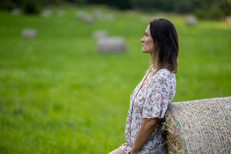 A beautiful woman surrounded by nature, posing on hay bales