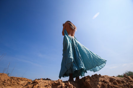 A Graceful Woman with Long Legs, Her Dress Dancing in the Wind Against the Skyの写真素材