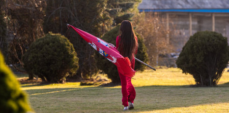 An elegant brunette in a red dress proudly poses, holding the wind-swept historical flag of Lithuaniaの写真素材