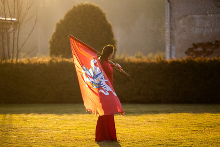 An elegant brunette in a red dress proudly poses, holding the wind-swept historical flag of Lithuaniaの写真素材