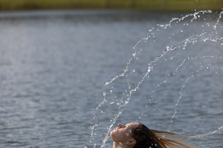 Energetic Hair Flip and Sparkling Water Splash â Beautiful Woman Enjoying a Summer Day in Natureの写真素材