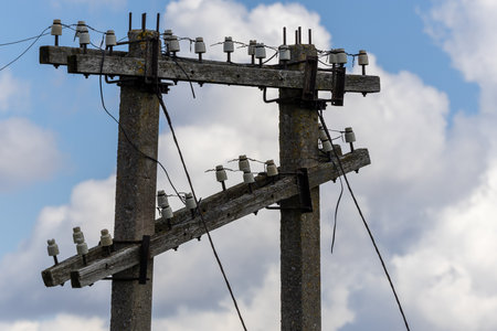 Old electricity poles with disconnected wires under a cloudy sky. The weathered concrete structures...