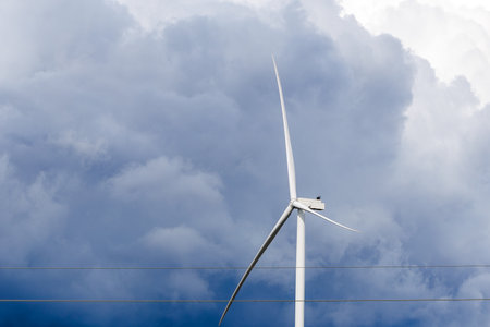 A modern wind turbine stands tall against a dark and cloudy stormy sky. Renewable energy symbolizing...