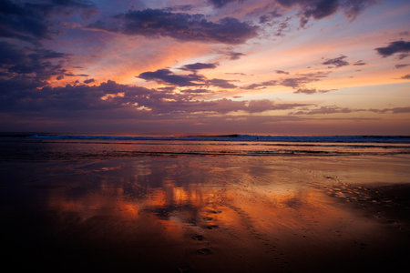 Vibrant sunset sky reflecting on wet sand along the shoreline. Dramatic clouds and glowing colors...