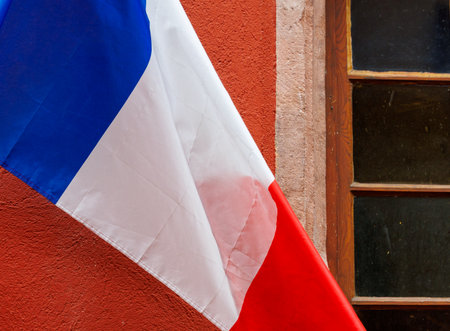 The French tricolor flag waving in front of historic architecture. Symbol of France, patriotism, and national pride. Perfect for politics, travel, culture, history, and European themesの写真素材