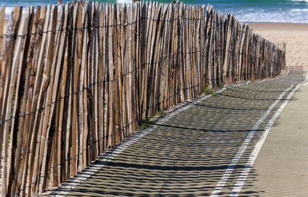 Traditional wooden sand dune fence along the Atlantic Ocean coastline in France. Rustic barrier used to protect dunes from erosion, with sand, grass and blue sea in the background on a sunny dayの写真素材
