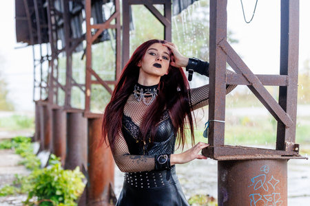 A gothic fashion model with long red hair, black leather clothing and dark makeup poses in an...