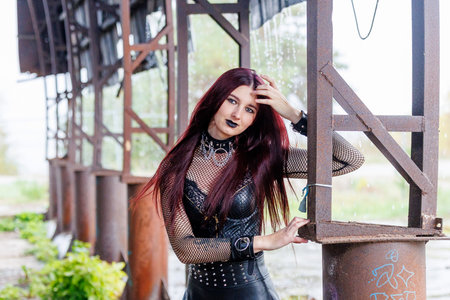 A gothic fashion model with long red hair, black leather clothing and dark makeup poses in an...