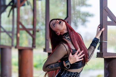 A gothic fashion model with long red hair, black leather clothing and dark makeup poses in an...