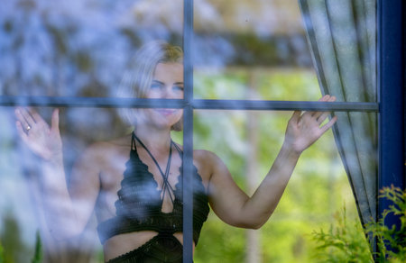 A woman framed behind glass, blending softness, mystery and nature. Light, reflections and silence create an intimate moment between the outside world and her inner thoughtsの写真素材