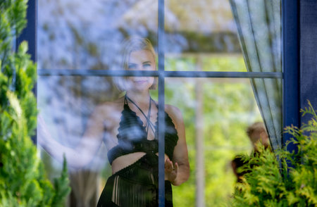 A woman framed behind glass, blending softness, mystery and nature. Light, reflections and silence create an intimate moment between the outside world and her inner thoughtsの写真素材