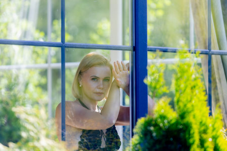 A woman framed behind glass, blending softness, mystery and nature. Light, reflections and silence create an intimate moment between the outside world and her inner thoughtsの写真素材